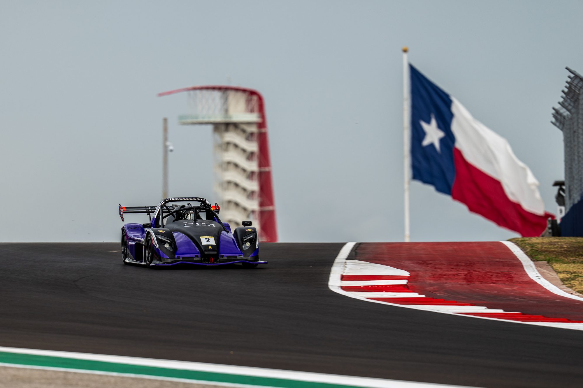 Purple Radical in front of the COTA tower and a Texas flag